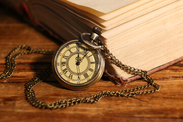 Pocket clock with chain and book on wooden table, closeup