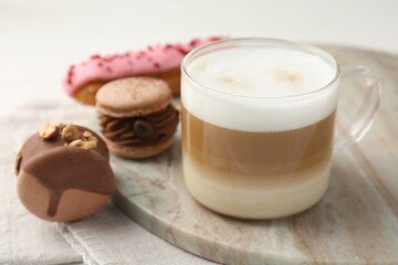 Aromatic coffee in cup, tasty macarons and eclair on table, closeup