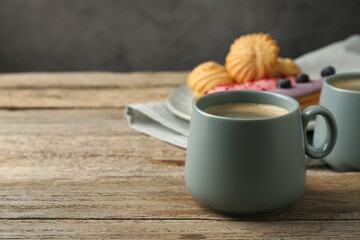 Aromatic coffee in cups, tasty eclairs and profiteroles on wooden table, space for text