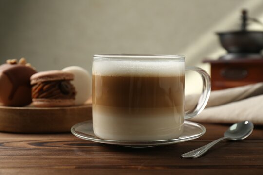 Aromatic coffee in cup, macarons and spoon on wooden table, closeup