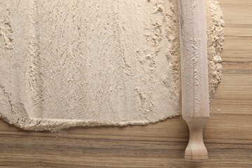 Flour and rolling pin on wooden table, top view