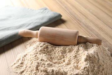 Pile of flour and rolling pin on wooden table, closeup