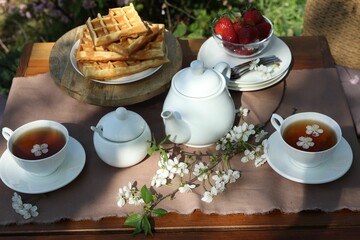 Beautiful spring flowers, freshly baked waffles and ripe strawberries on table served for tea drinking in garden