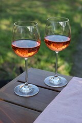 Glasses of rose wine on wooden table in garden