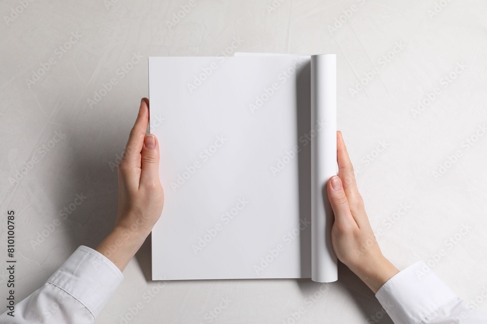 Wall mural woman holding notebook with blank pages at white table, top view. mockup for design