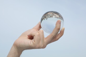 View of beautiful city street, overturned reflection. Man holding crystal ball against sky, closeup
