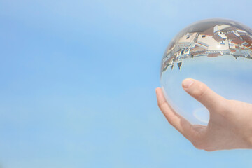 View of beautiful city street, overturned reflection. Man holding crystal ball against sky,...