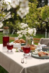 Stylish table setting with beautiful spring flowers, fruit drink and pie in garden