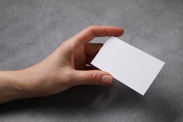 Woman holding blank card at grey table, closeup. Mockup for design