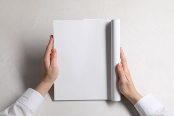 Woman holding notebook with blank pages at white table, top view. Mockup for design