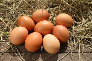 Fresh chicken eggs and dried hay on wooden table
