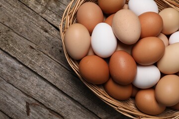 Fresh chicken eggs in wicker basket on wooden table, top view. Space for text