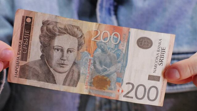 Person holding a 200 srb banknote with their thumb and finger, serbian dinar close up.