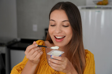 Attractive smiling young woman eating yogurt natural in the kitchen at home