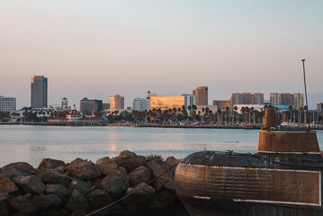 Evening coastal scene with warm hues on buildings, palm trees lining the waterfront. Skyline of mid...