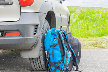 two backpacks stand at the rear wheel of an SUV parked at a campsite. Traveling by car. Close-up.