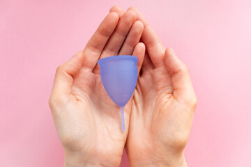 Woman hands carefully holding blue menstrual cup, showcased against soft pink background to emphasize eco-friendly menstrual care.