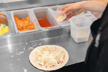 Pizzamaker worker preparing fresh food pizza adds toppings with mozzarella cheese, top view....