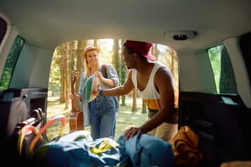 Happy couple packing up camping equipment in trunk of  van in nature.