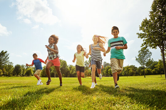 Happy kids, diversity and running with friends in nature for fun, playful day or summer at park. Group of excited children or youth enjoying sunny outdoor holiday or weekend on grass field together