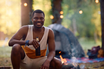 Happy black camper drinking beer and looking at camera.