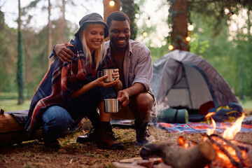 Happy couple relaxing by  fire while camping in woods.