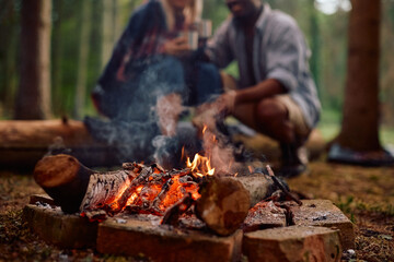 Fototapeta premium Close up of campfire with couple in background.