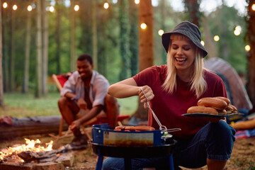 Happy woman grilling sausages on camping in nature.