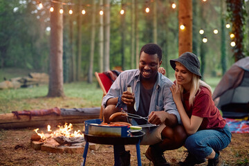 Young happy couple making barbecue while camping in forest.