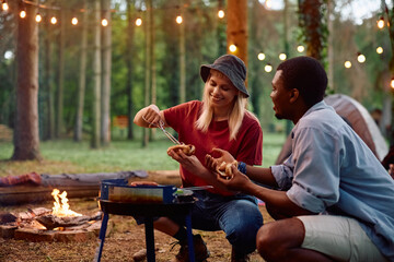 Happy couple making hot dogs on camping in nature.