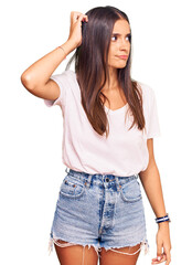 Obraz premium Young hispanic woman wearing casual white tshirt confuse and wondering about question. uncertain with doubt, thinking with hand on head. pensive concept.