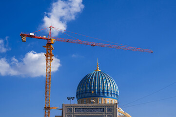 Center of Islamic Civilization in Tashkent, Uzbekistan. Crane on a construction site builds a dome of new large muslim mosque against a blue sky background