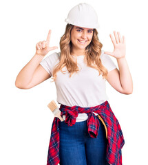 Young caucasian woman wearing security helmet showing and pointing up with fingers number seven while smiling confident and happy.