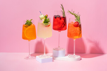 4 glasses with alcoholic cocktails on podiums on pink background.