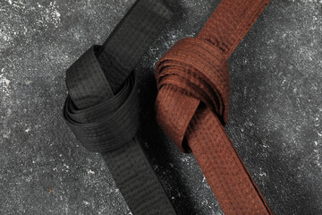 Black and brown karate belts on gray textured background, flat lay