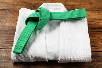 Green karate belt and white kimono on wooden background