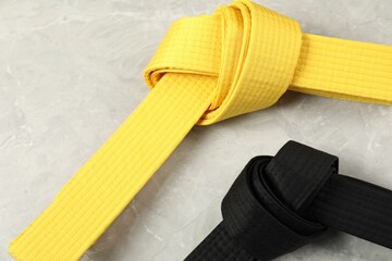 Black and yellow karate belts on gray marble background, closeup