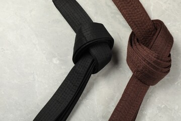 Black and brown karate belts on gray marble background, flat lay. Space for text