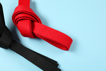 Red and black karate belts on light blue background, flat lay. Space for text