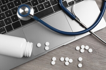 Laptop, stethoscope, pills and bottle on wooden table, flat lay