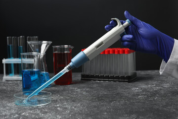 Laboratory analysis. Scientist dripping sample with micropipette into petri dish at grey table, closeup