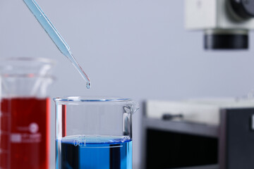 Dripping liquid from pipette into beaker in laboratory, closeup. Space for text