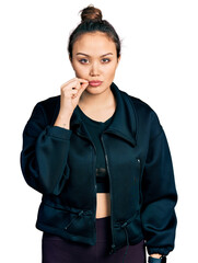 Young hispanic girl wearing sportswear mouth and lips shut as zip with fingers. secret and silent,...