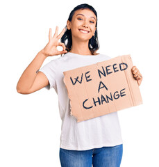 Young woman holding we need a change banner doing ok sign with fingers, smiling friendly gesturing excellent symbol