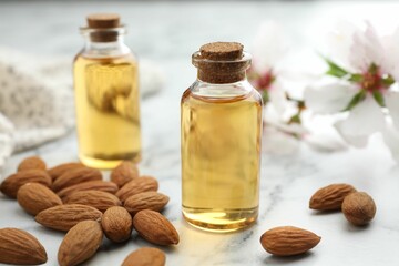 Almond oil in bottles and nuts on white marble table, closeup