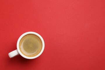 Aromatic coffee in cup on red background, top view. Space for text