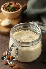 Fresh almond flour in jar and nuts on wooden table, closeup