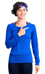 Beautiful young woman with short hair wearing training workout clothes cheerful with a smile on face pointing with hand and finger up to the side with happy and natural expression