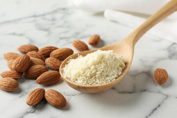 Spoon with fresh almond flour and nuts on white marble table, closeup
