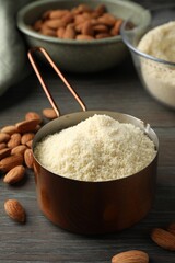 Fresh almond flour in scoop and nuts on wooden table, closeup